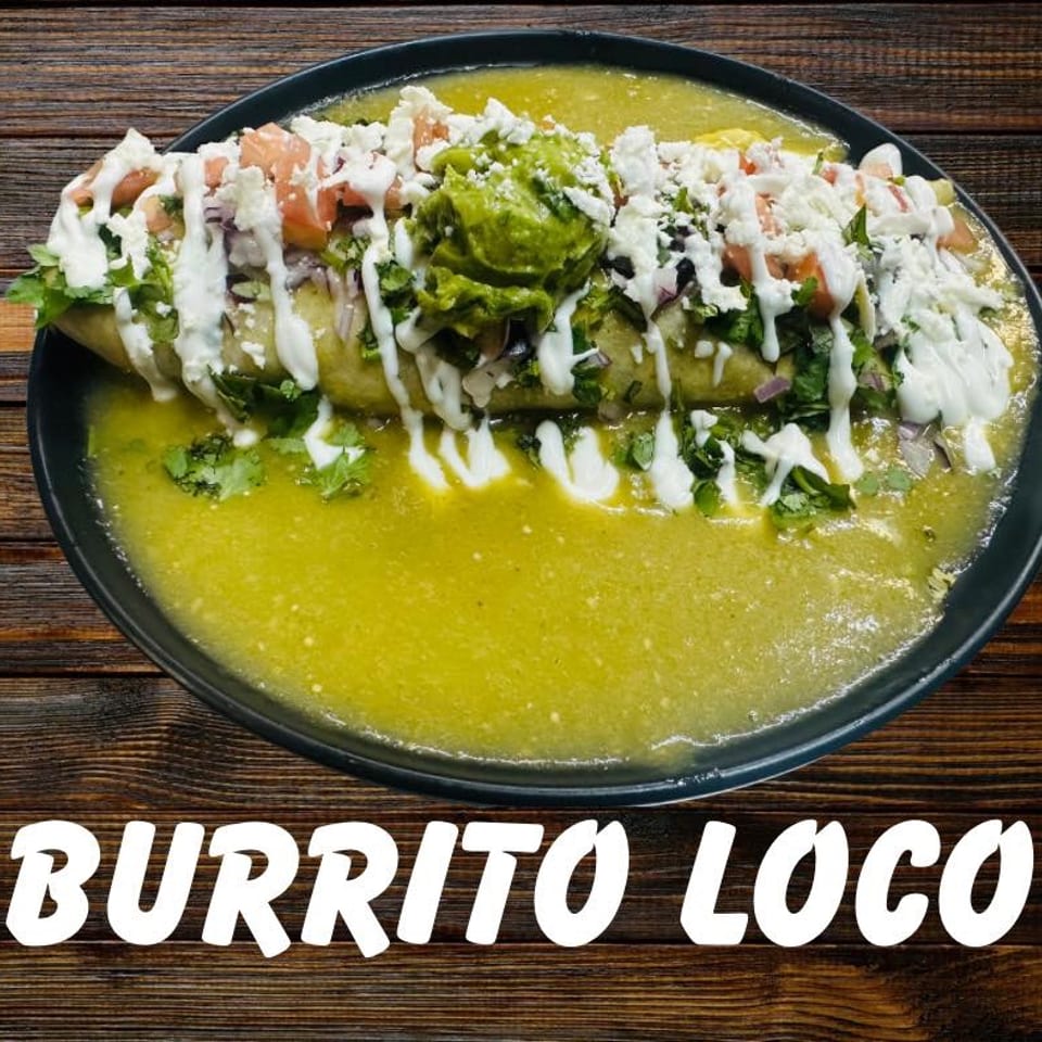 A large burrito covered in green sauce, guacamole, cheese, and pico de gallo.