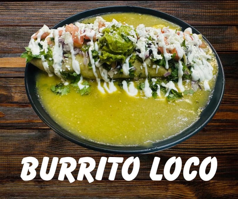 A large burrito covered in green sauce, guacamole, cheese, and pico de gallo.